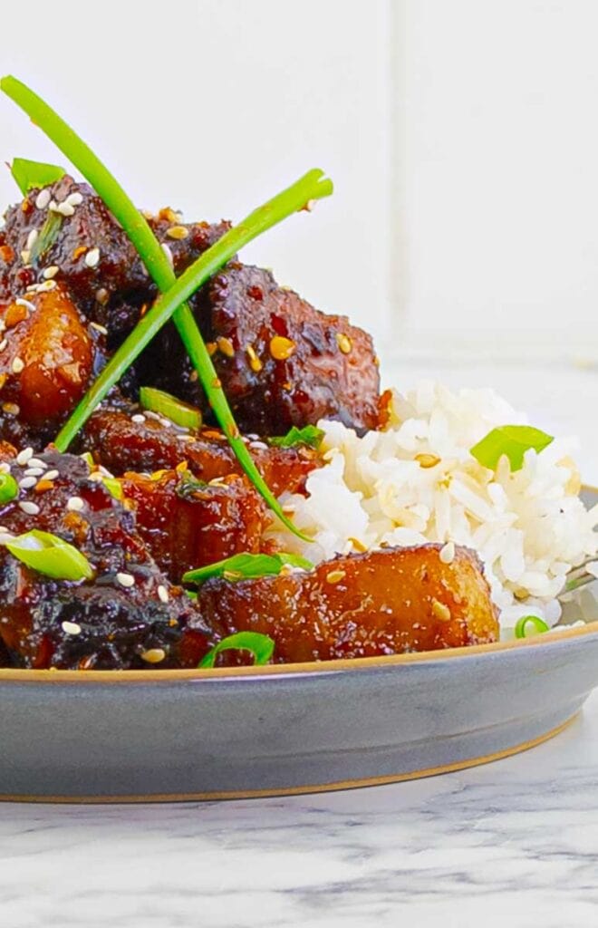 Sticky Chinese Pork Belly with white rice on a gray plate